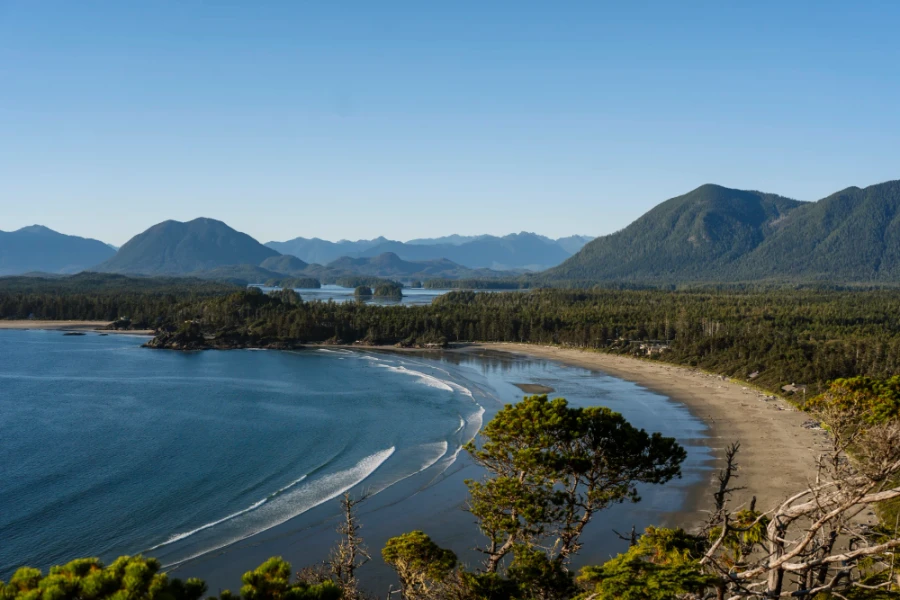 large waves crashing on the sandy shores of Cox Bay with mountains in the distance in Tofino, BC