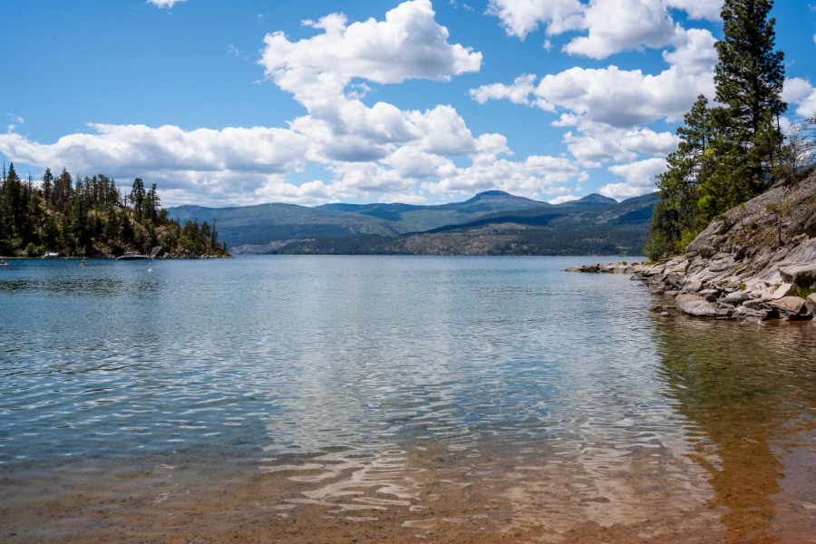The calm blue waters of Kalamaka Lake bordered by the tree-covered stony shores near Ellison Provincial Park