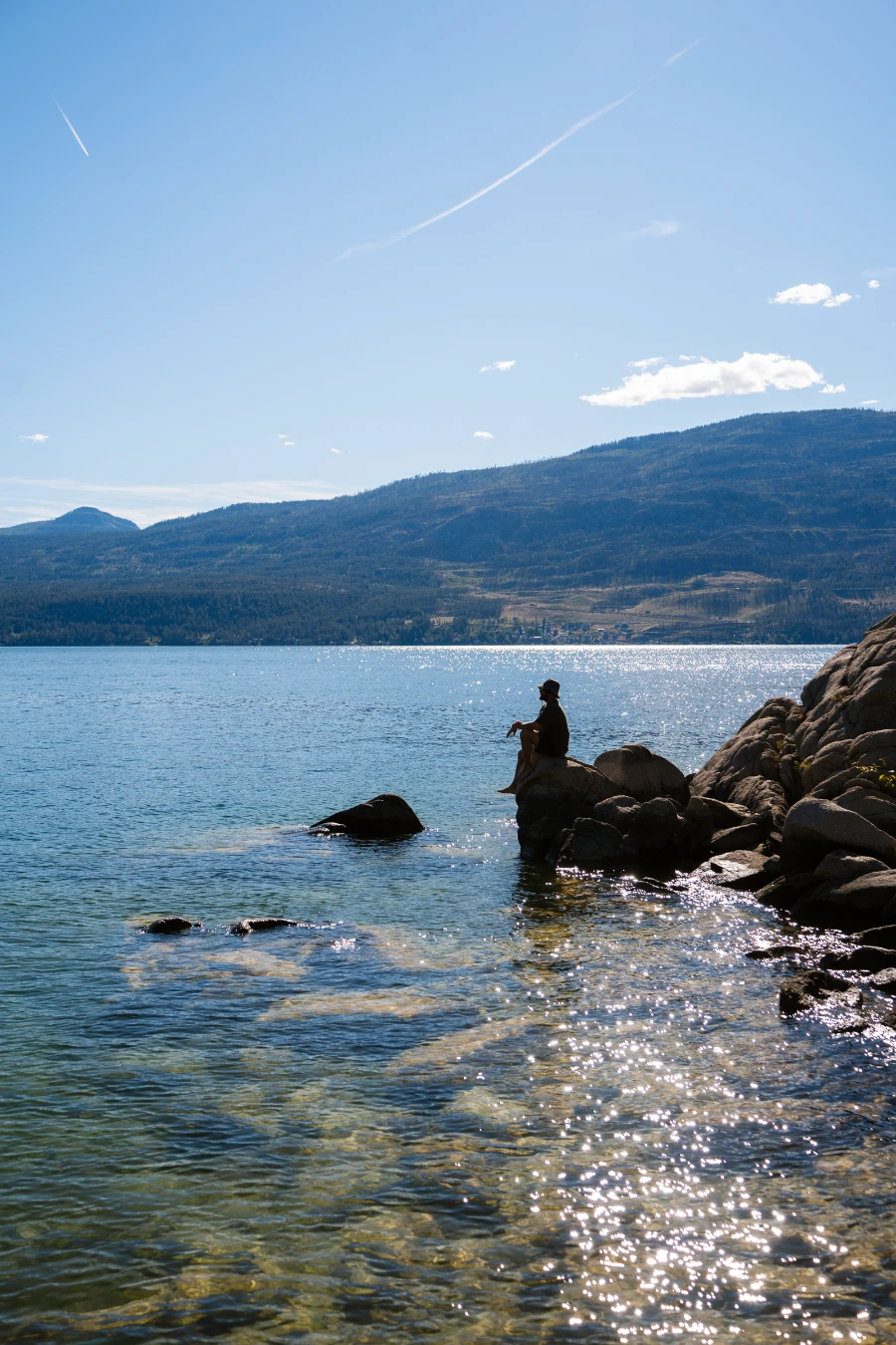 A man sits on a boulder on the shore of the calm waters of Ellison Bay