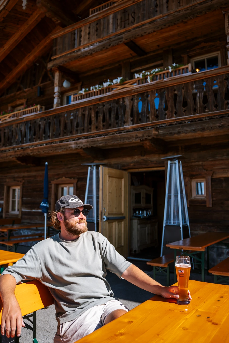 A man sits at a wooden table holding a pint of beer in front of an Austrian-style building