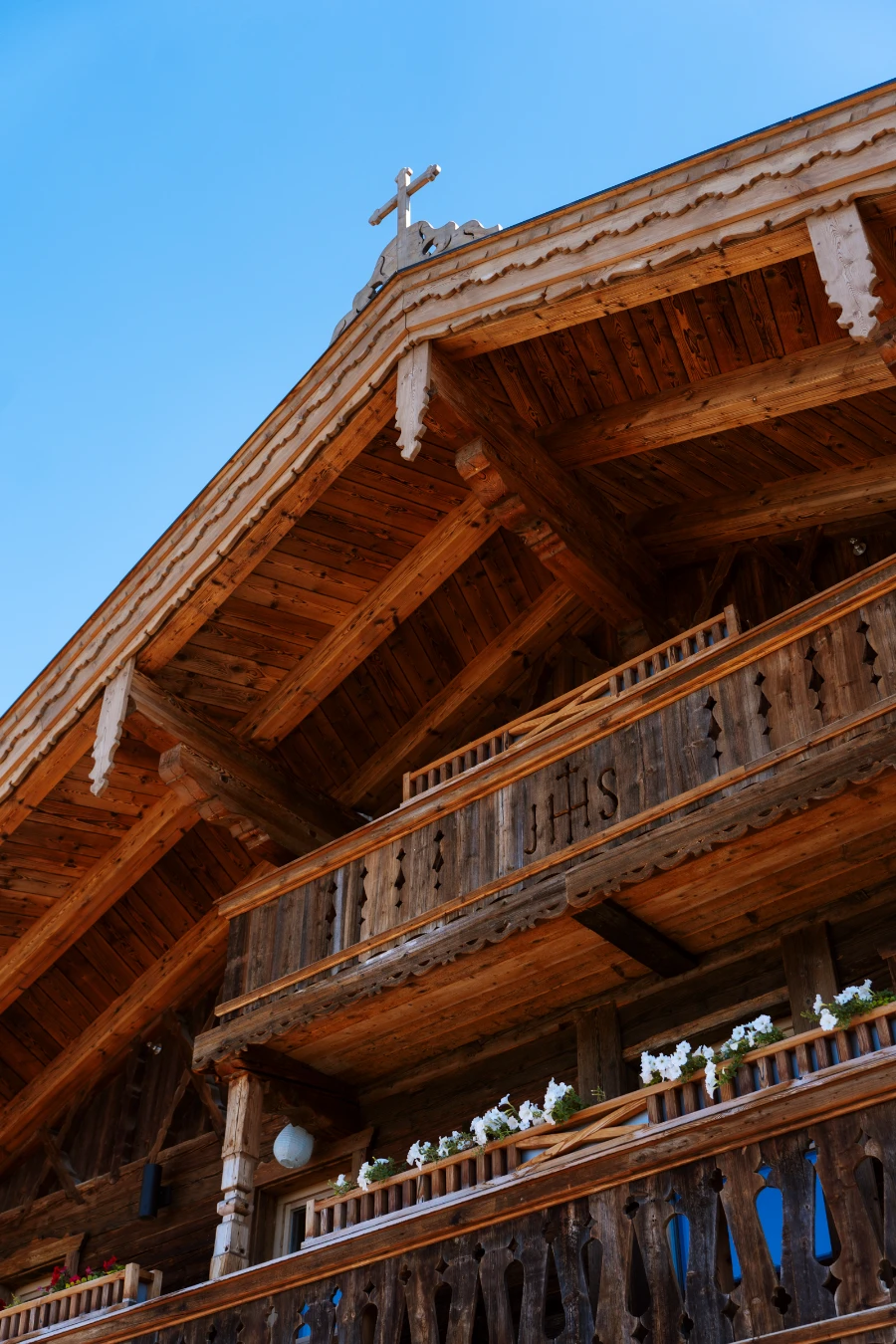A multi-storied Austrian-style farmhouse has flower baskets hanging on the railing of the middle floor’s balcony