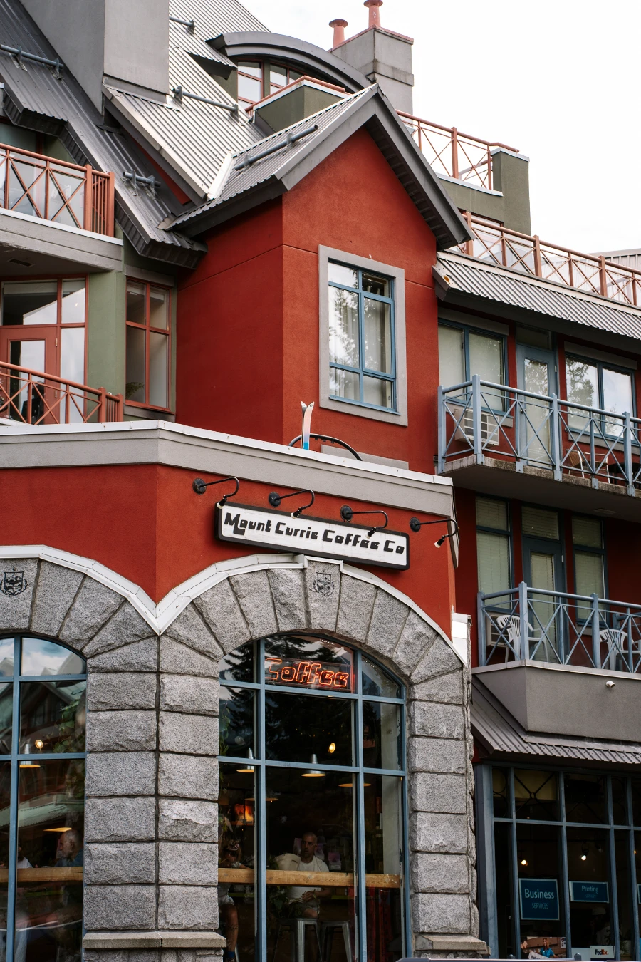 A large white sign above a stone arch reads ‘Mount Currie Coffee Co.’ and a red lit neon sign inside the window below the arch reads ‘Coffee’