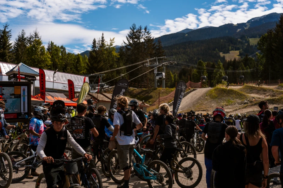 Several mountain bikers queuing along the metal partitions leading to the Fitzsimmons Express in Whistler while other bikers come down the berms behind them