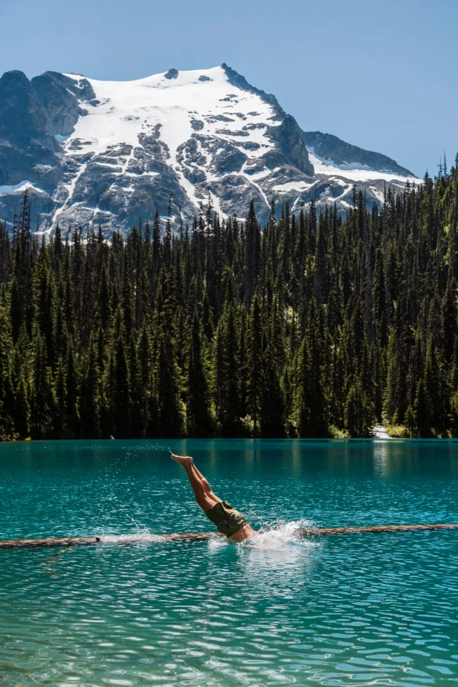 A man diving off of a floating log into the clear blue waters of Joffree Lake near Pemberton