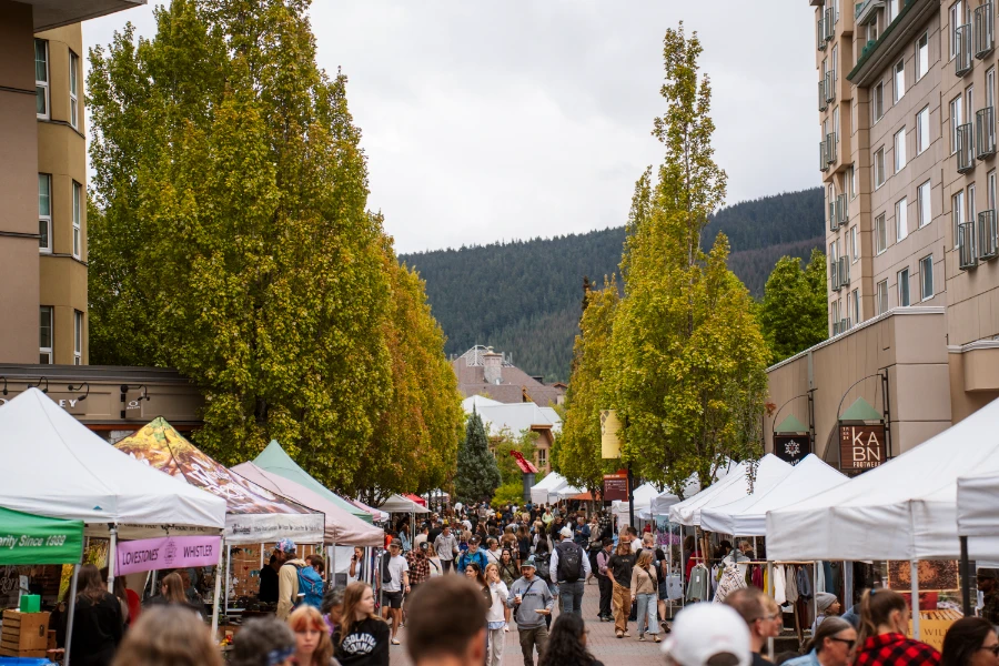A huge crowd of people wander along the pedestrian streets of Whistler that are lined with white tents that house the vendors of the Whistler Farmers Market