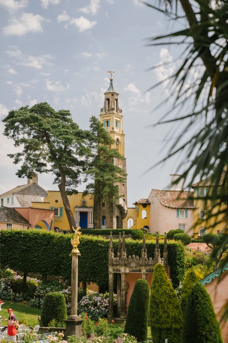 A large European style bell tower looms over a lush and manicured garden in Portmeirion, Wales