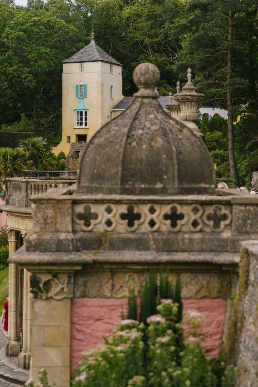 An ornate stone done partially obscures the view of more pastel buildings beyond it in Portmeirion, Wales