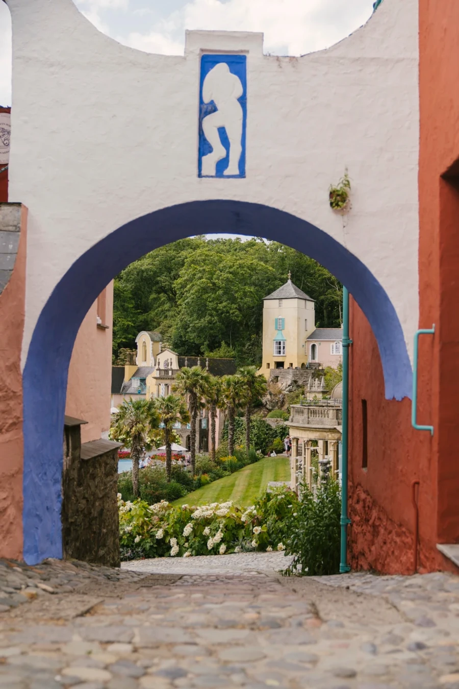 A cobble stone lane leads through a colorful stone archway into an Italian style village in Portmeirion, Wales