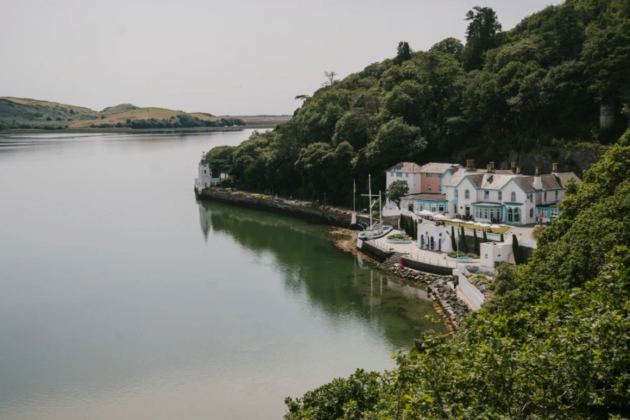 A coastal path built along a sea wall runs along the sea side and past a large multi-colored building with a boat docked in front of it in Portmeirion, Wales