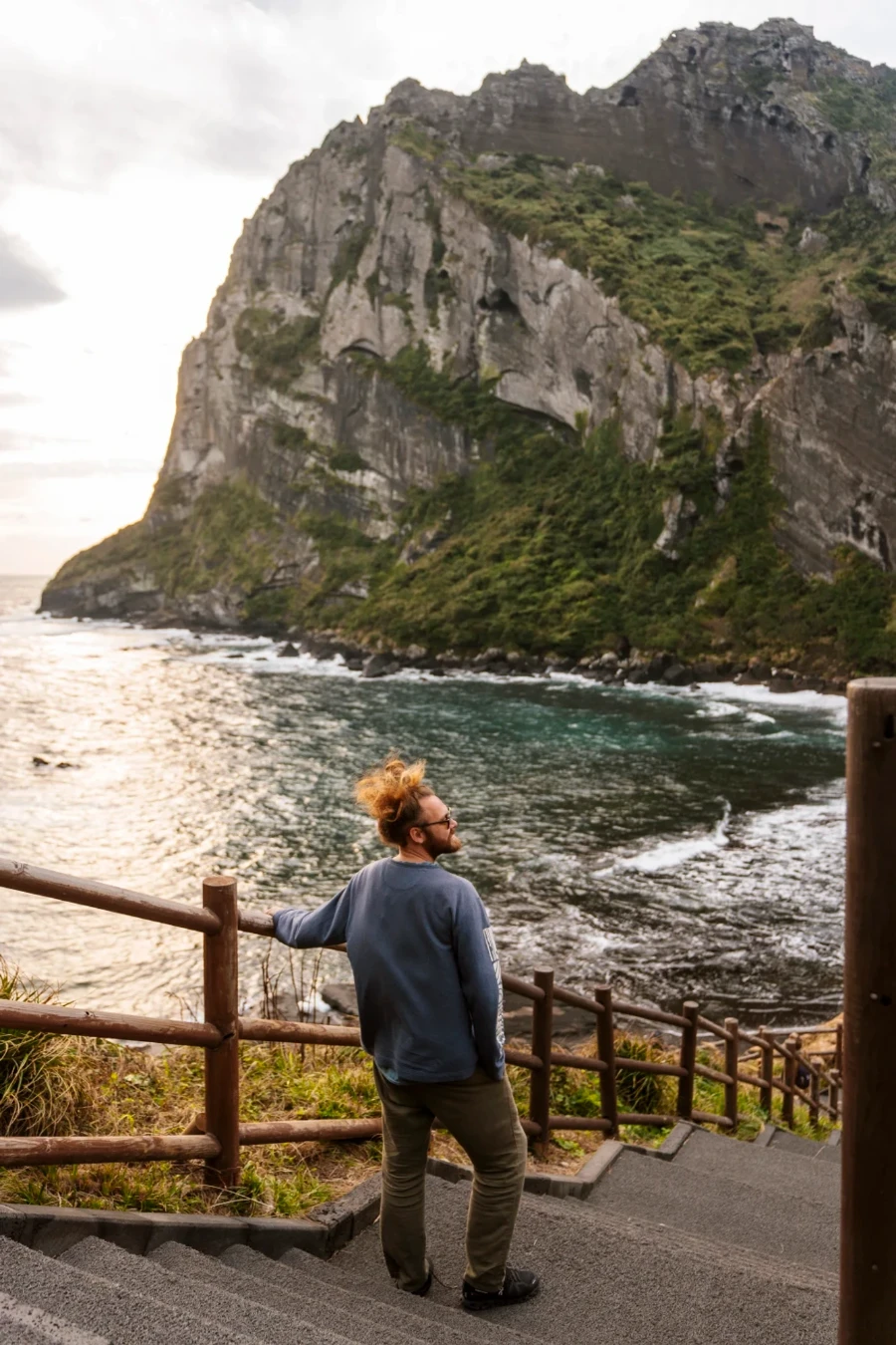 Man leaning on a wooden railing on steps leading down to Seongsan Ilchulbong on Jeju Island, South Korea