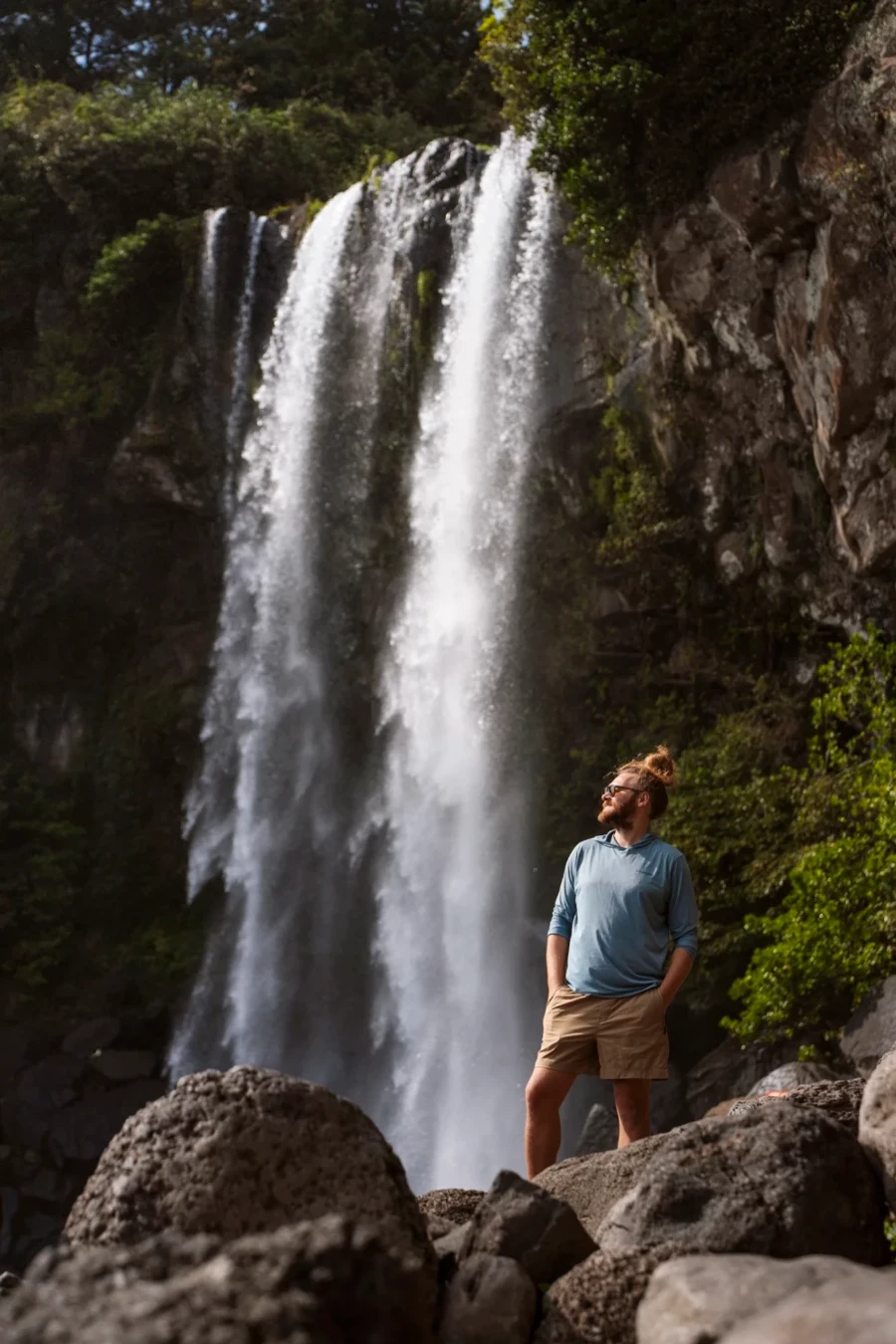 A man stands below a powerful waterfall on Jeju Island, South Korea