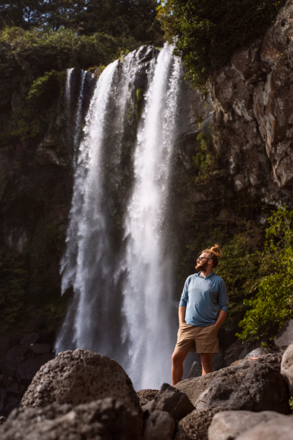 A man stands in front of a powerful waterfall on Jeju Island