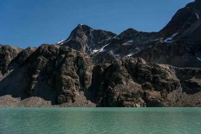 The steep cliffs of Wedge Mountain descending into the clear blue waters of an alpine lake
