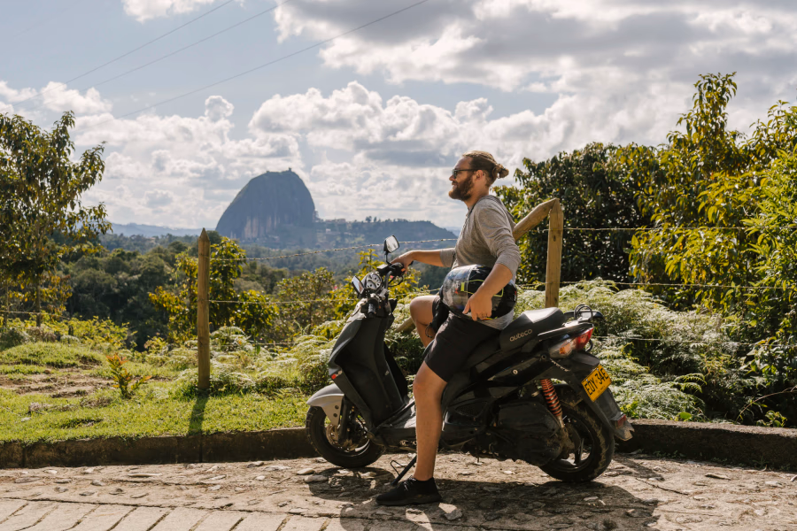 Things to Know Before Visiting Guatape: Man on scooter with El Penol rock in the distance