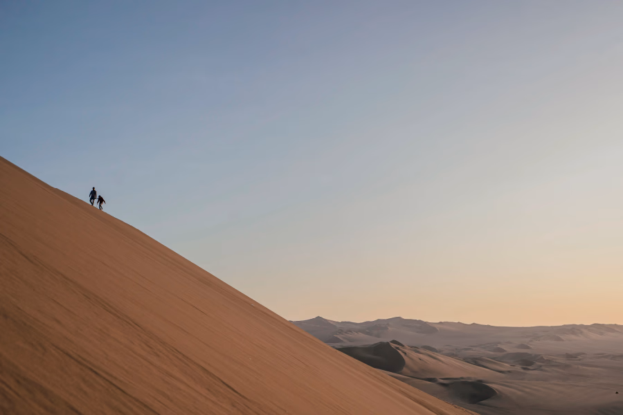 Best Things to Do In Huacachina, Peru: two people hiking a large dune