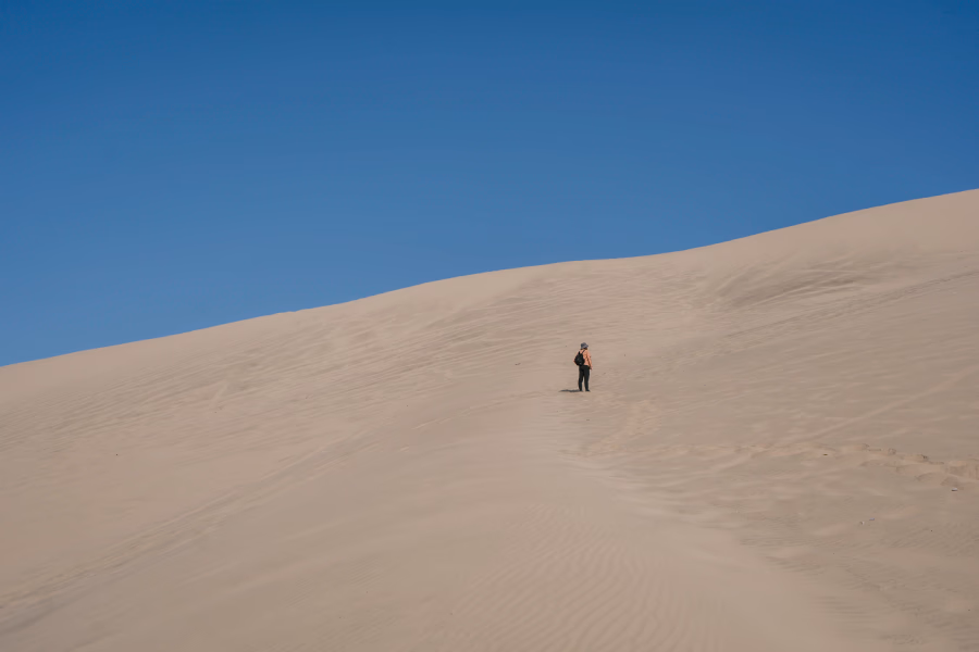Best Things to Do In Huacachina, Peru: man hiking up a large sand dune