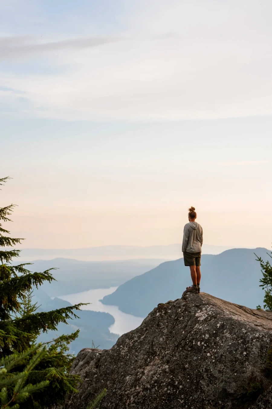 Man standing on a large rock near the peak of Tin Hat mountain on the Sunshine Coast, BC