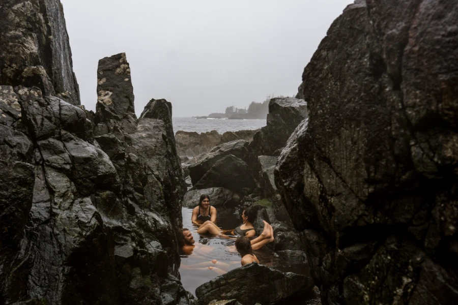 A group of 4 people sit in a circle in a natural rock pool surrounded by huge rock walls