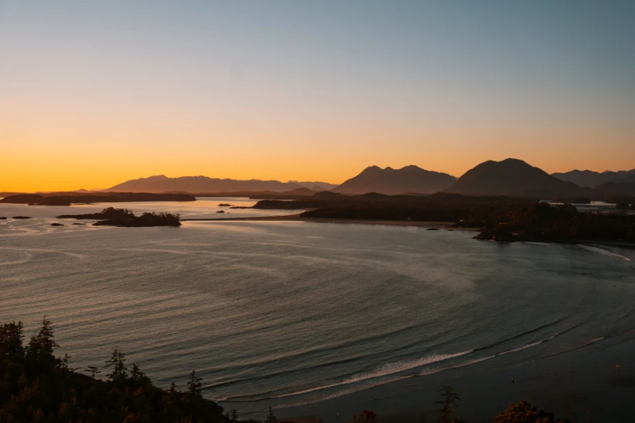 Dozens of rows of waves roll into a crescent shaped bay with distant mountains lit by the setting sun