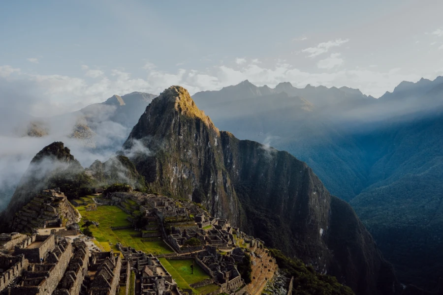 Sunrise light streaks over unseen mountain peaks and illuminates the mountains and ruins of Machu Picchu