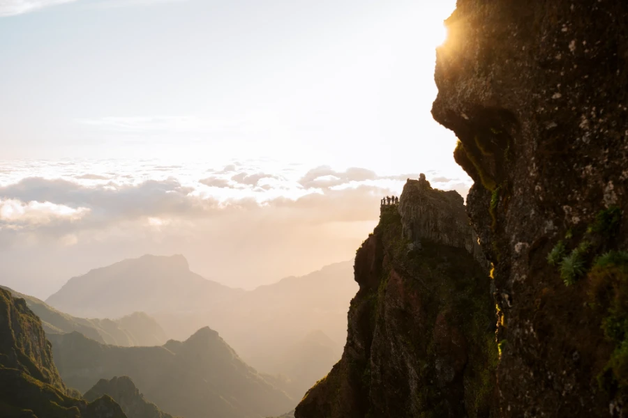 The sun flares around the jagged edge of a cliff with more jagged pillars rising high above a misty valley on the Island of Madeira, Portugal