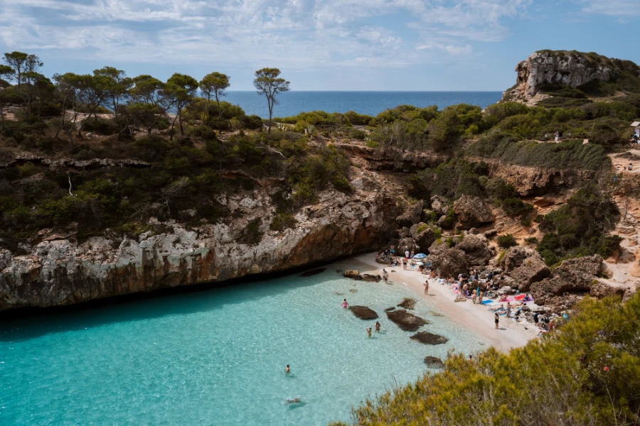 A rectangular channel of shallow turquoise water that shimmers and shows the white sand below it, bordered on all sides by stone cliffs covered in short bushes