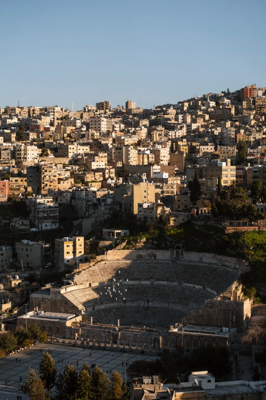 A large public square in front of a Roman era theatre that is surrounded by the sprwaling neighbourhoods of Amman
