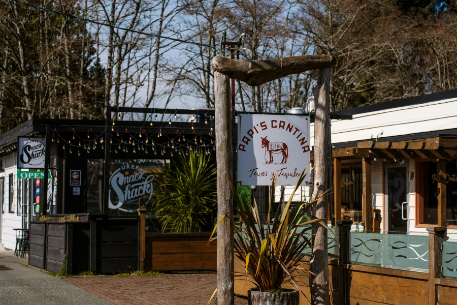 Signs hang over the side walk with one reading Papi's Cantina and the other Ukee Snack Shack in Ucluelet, BC