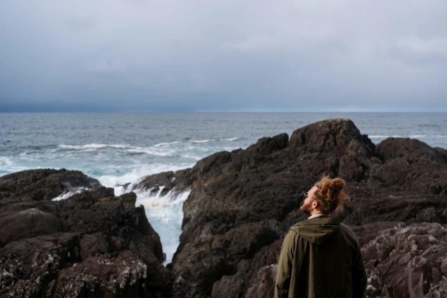 A man stands in front of a rocky shore that is being hit by choppy waves