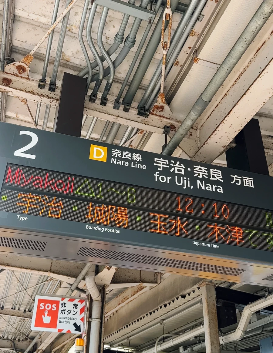 A neon sign shows the next time for a train to Uji from Kyoto, Japan