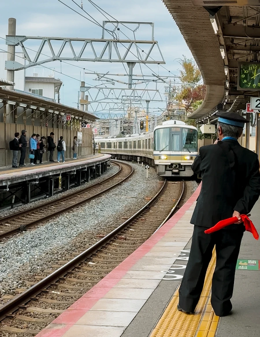 A uniformed man blows a whistle and holds a flag while a train pulls into Kyoto station