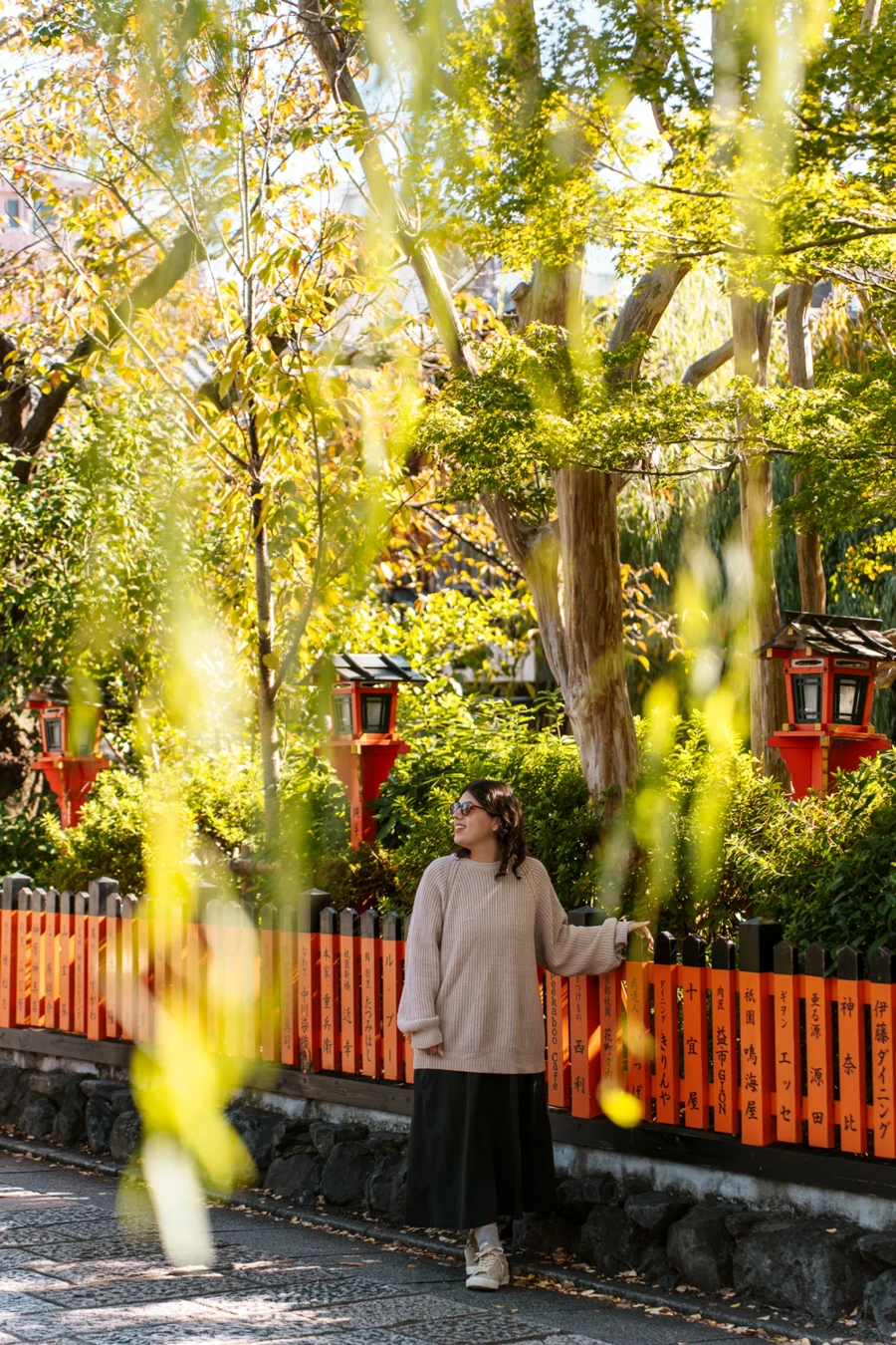 A woman leans on an orange painted fence in the Gion neighbourhood in Kyoto, Japan