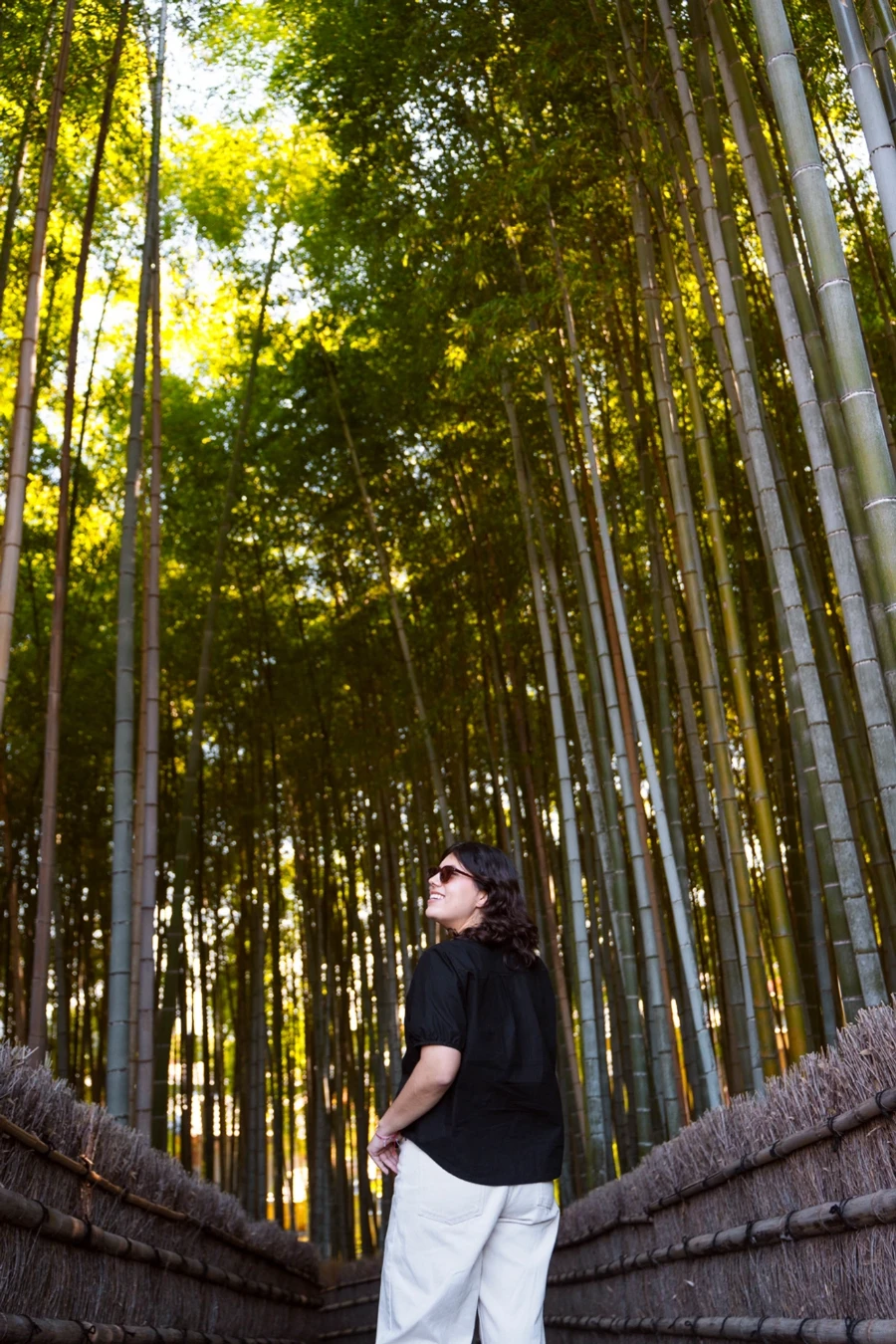 A woman stands in an empty path that weaves through a bamboo grove in bamboo grove in Arashiyama, Japan