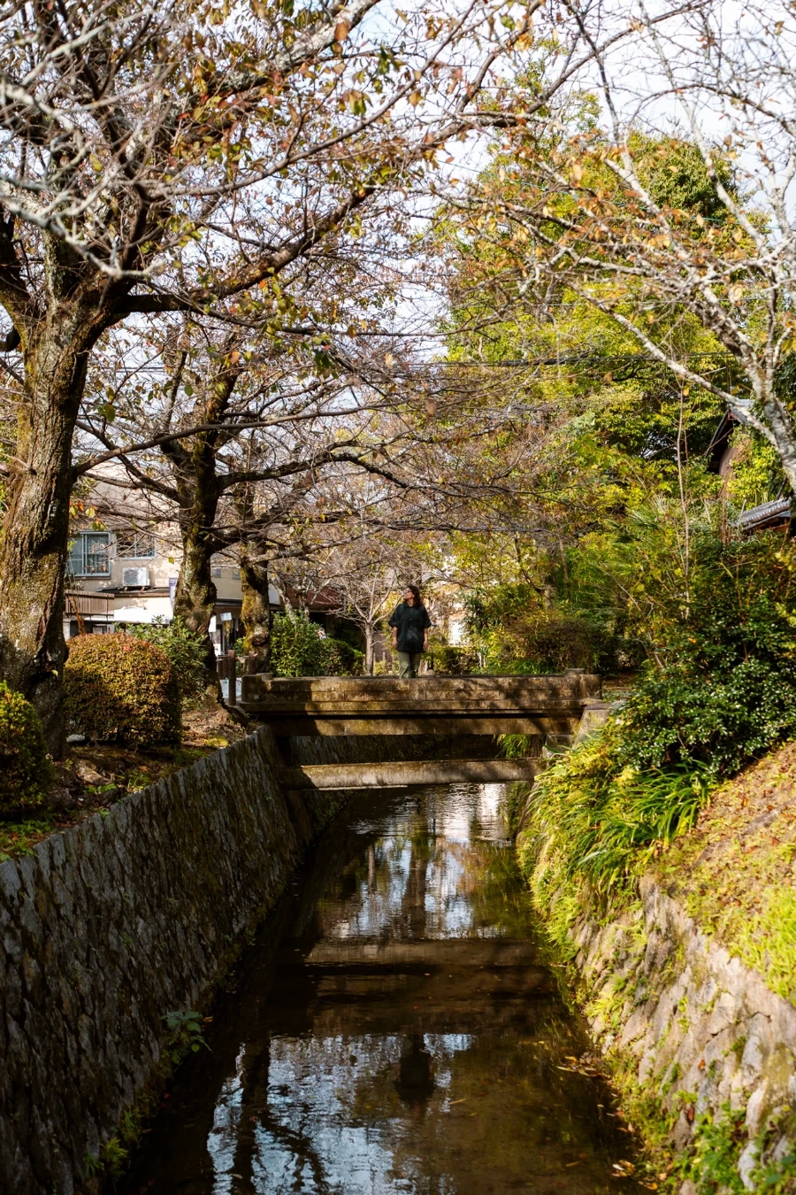 A woman stands on a stone bridge above a river near the Philosopher's Path in Kyoto, Japan
