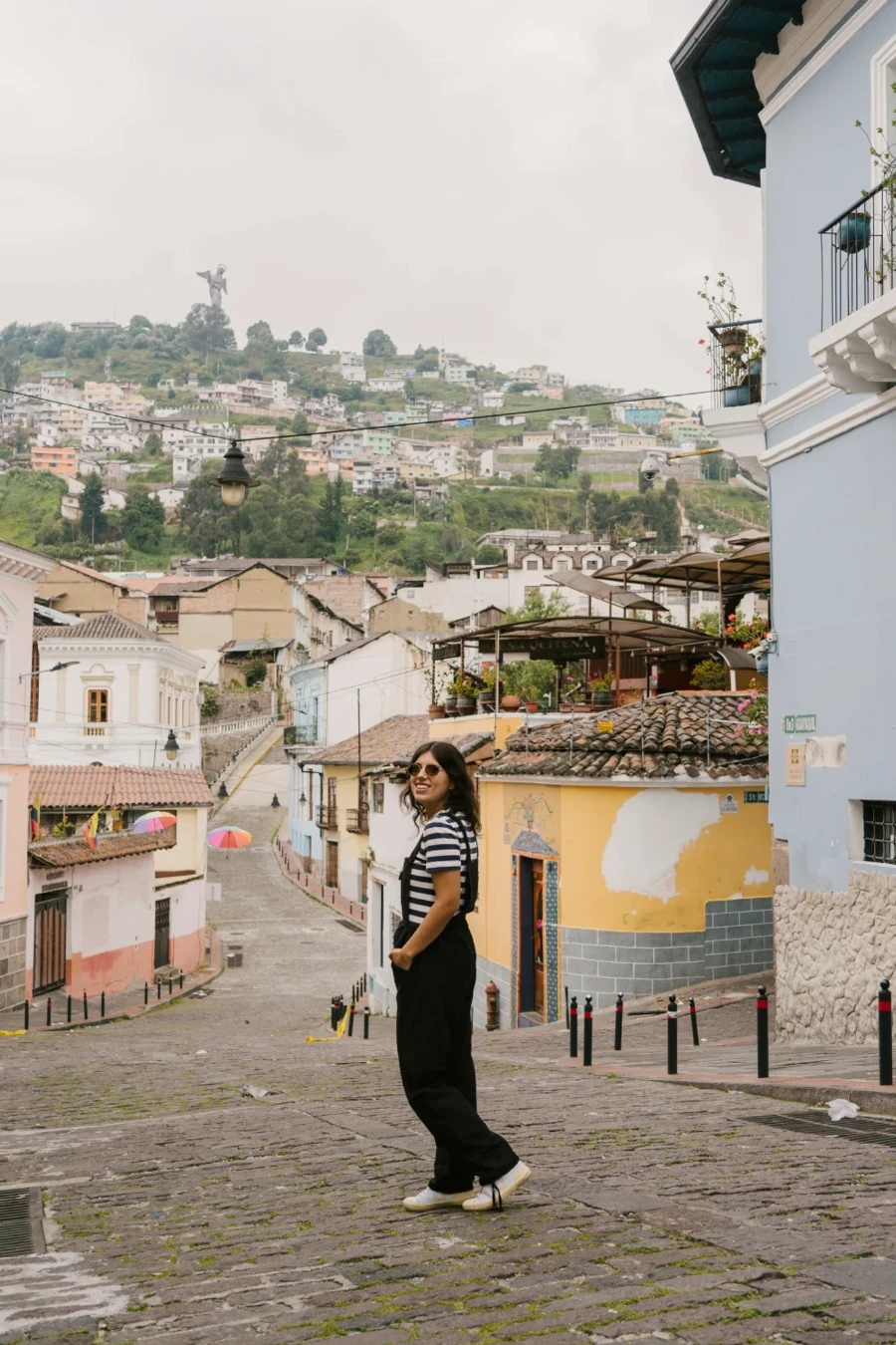 A woman standing on a cobblestone street in front of a view of El Panecillo