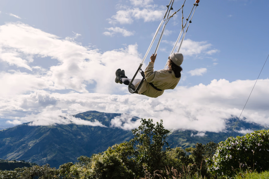 A woman swings on a swing in front of cloud covered mountains at La Casa del Árbol