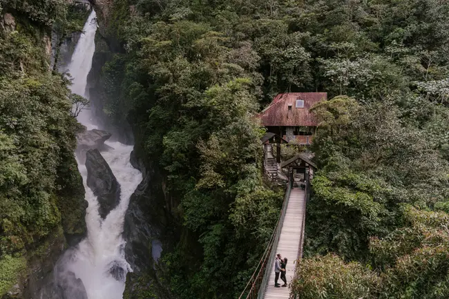 A man and woman embrace in the middle of a suspension bridge with a large powerful waterfall behind them