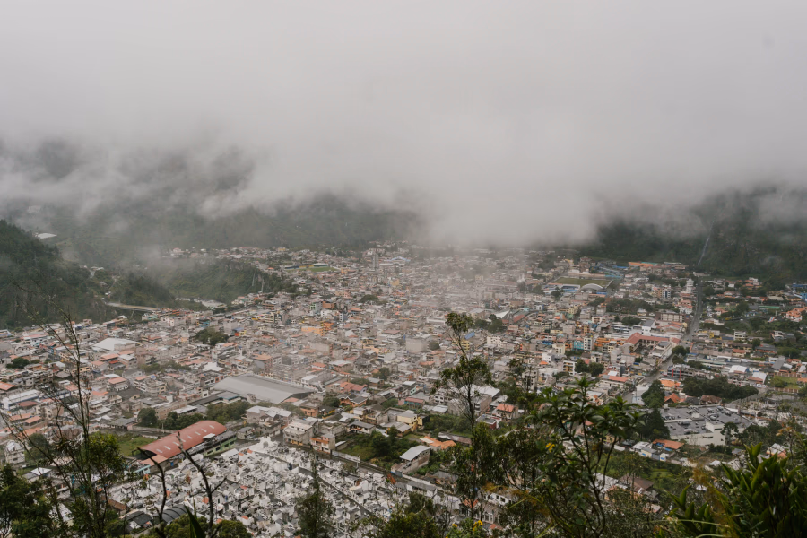 A densely populated city built in a lush green valley surrounded by clouds and mountains