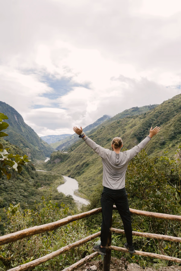 A man stands with his arms outstretched at a viewpoint above a large meandering river