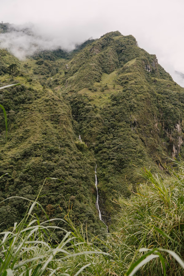 A tall waterfall cascades down a lush green mountain