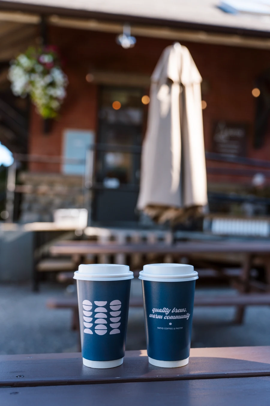 Two to-go coffees sitting on a wooden picnic table outside of Ratio Cafe & Bakery in downtown Vernon
