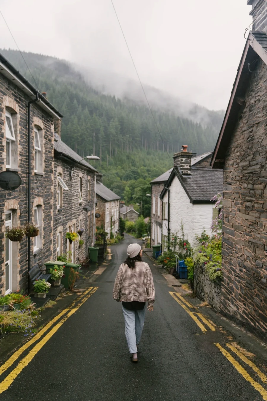 A woman walks down an empty street lined with stone cottages in Corris, Wales