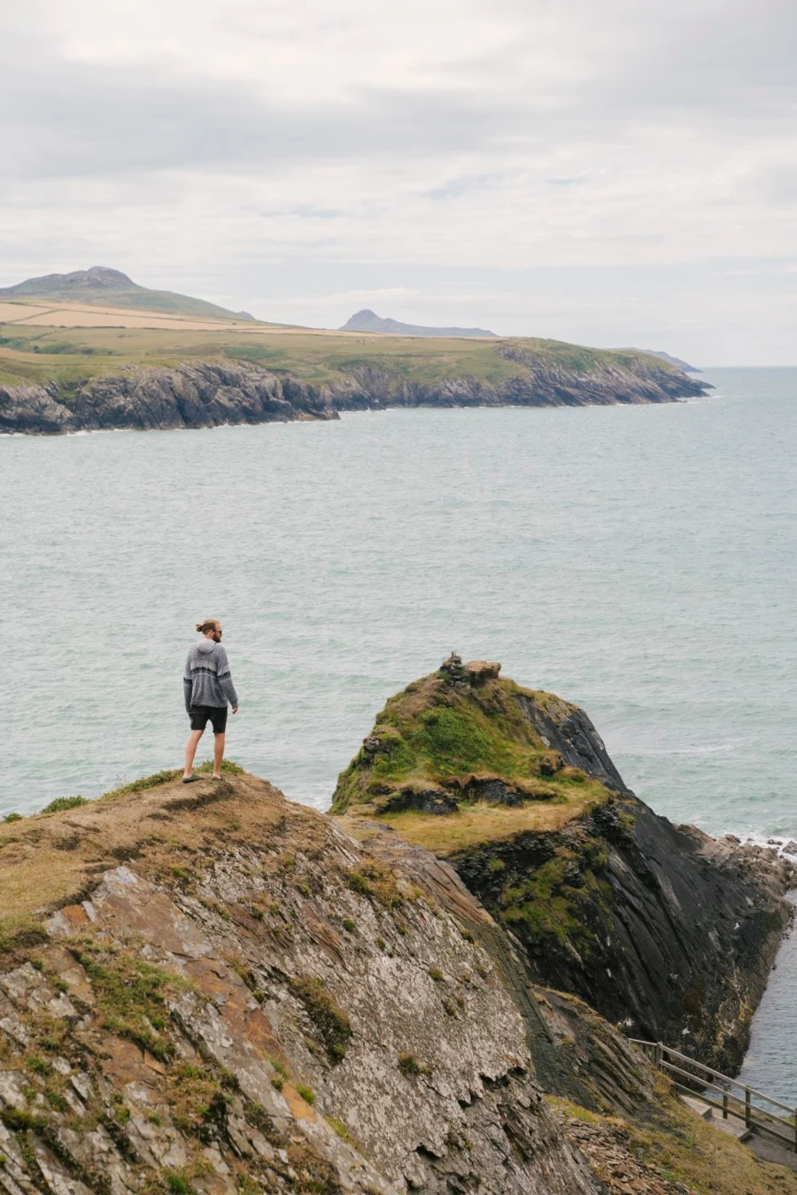 Man walking along a rocky cliff the juts out into the sea next to the Blue Lagoon, Wales