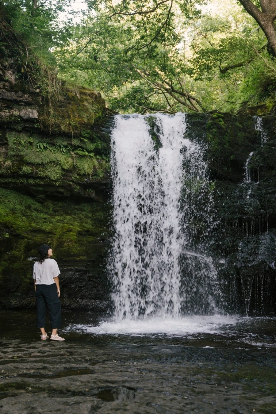 Woman standing beside a tall waterfall in Waterfall Country, Wales