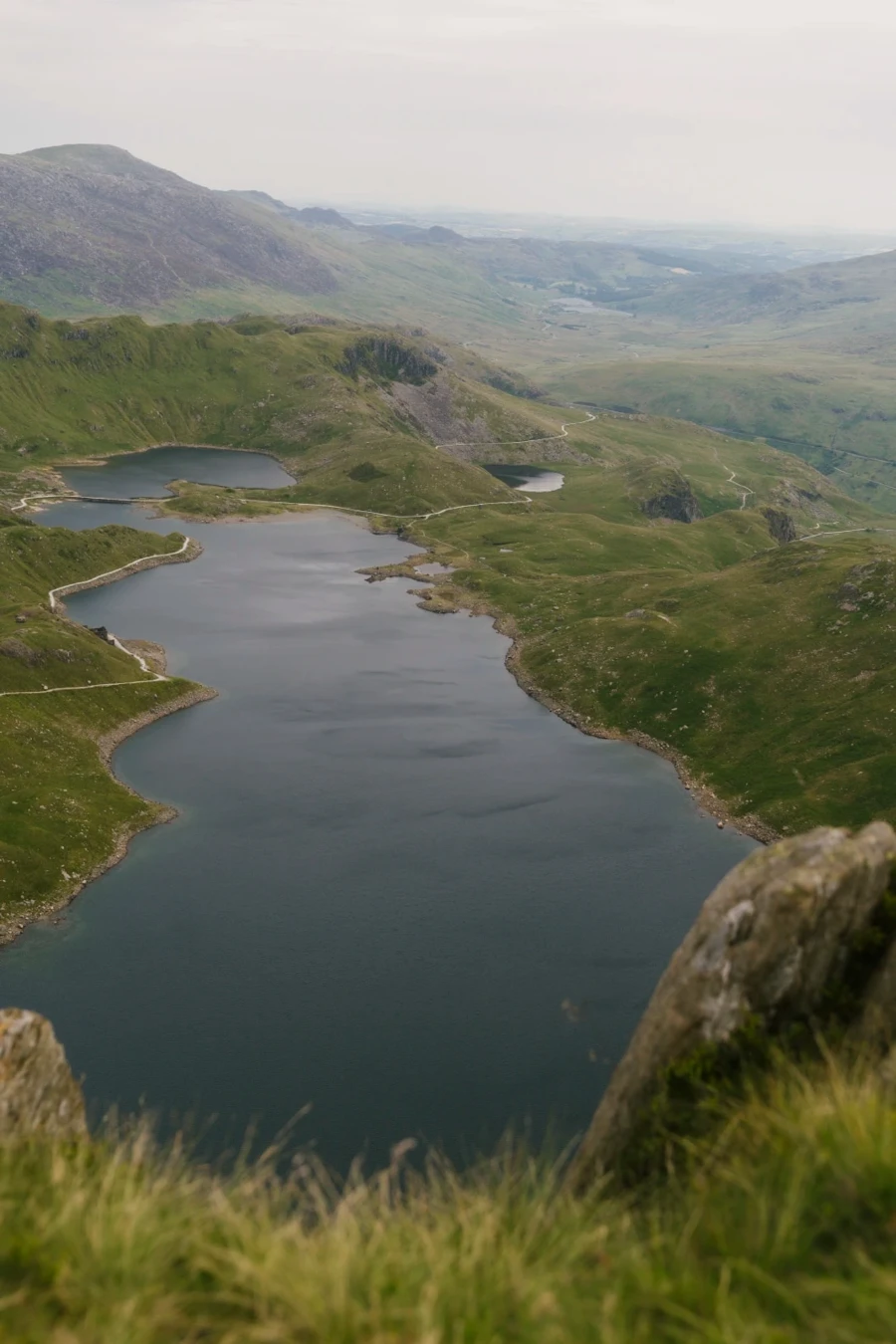 A large narrow lake surrounded on either side by rolling green hills
