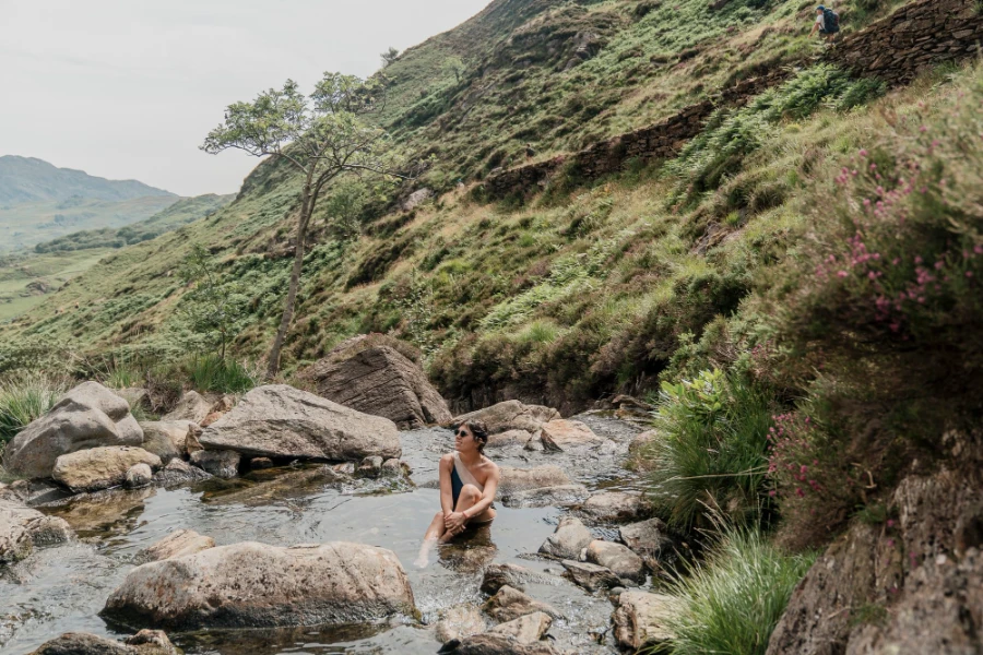 A woman sits in a shallow pool of water at Mount Snowdon Fairy Pools, Wales