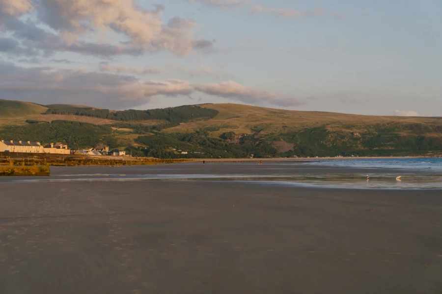 A row of houses look out to a wide sandy beach at sunset in Anglesey, Wales