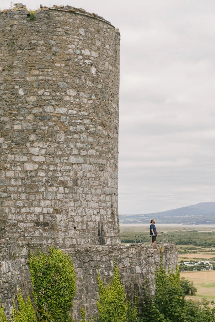 A man stands on a walkway beneath a large stone tower at Harlech Castle, Wales