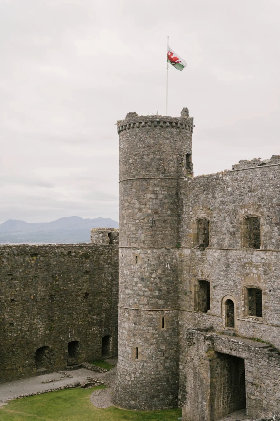 A large stone tower and wall surround a grassy coutyard at Harlech Castle, Wales