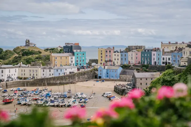 A row of multi-colored sea side houses with the sea behind them and a sandy beach with boats docked in front of them
